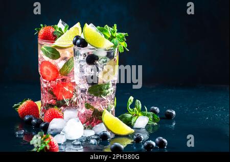 Cocktail Mojito di fragole e mirtilli con lime, rum bianco, soda, zucchero di canna, menta, e ghiaccio in vetro highball su fondo blu profondo. Estate Foto Stock