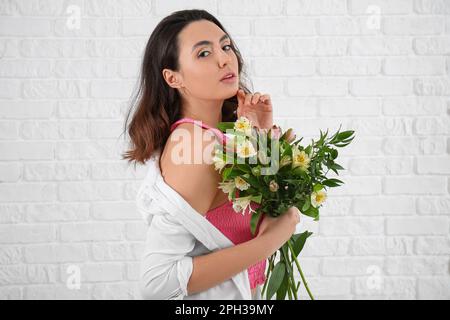 Giovane donna con fiori di alstroemeria su sfondo di mattoni bianchi Foto Stock