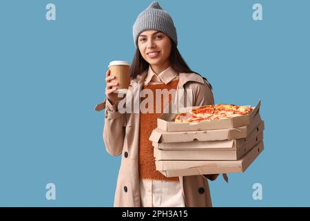 Giovane donna in cappello con tazza da caffè e scatole di gustosa pizza su sfondo blu Foto Stock