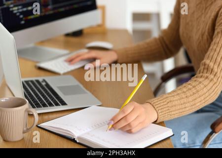 Giovane programmatore femmina che scrive in taccuino, primo piano Foto Stock