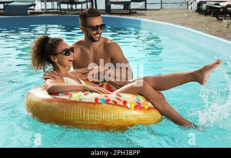 Felice coppia con anello gonfiabile in piscina all'aperto nelle giornate estive soleggiate Foto Stock