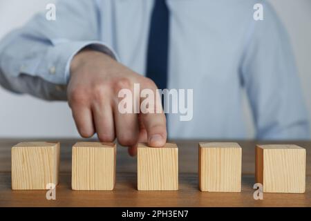 Uomo d'affari che organizza cubetti bianchi su un tavolo di legno, guardaroba. Spazio per il testo Foto Stock