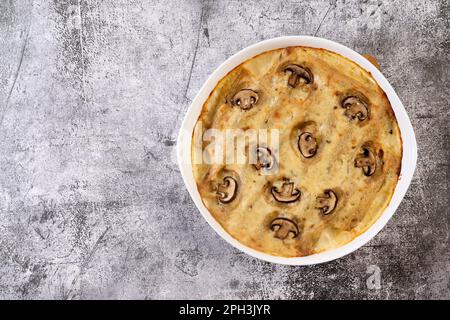 Cannelloni ripieni di carne e formaggio cotti in salsa di besciamella in una teglia bianca su fondo grigio scuro. Vista dall'alto, disposizione piatta Foto Stock