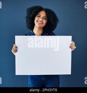 Siate i primi a saperlo. Studio di una giovane donna che tiene un cartello bianco su sfondo blu. Foto Stock