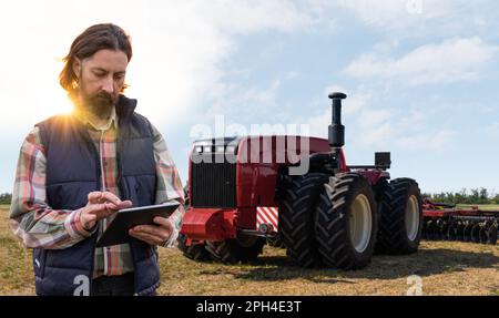 Un agricoltore con tablet digitale controlla un trattore autonomo in un'azienda agricola intelligente. Foto di alta qualità Foto Stock