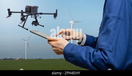 Ingegnere con computer tablet controlla drone su uno sfondo di turbine eoliche. Foto di alta qualità Foto Stock