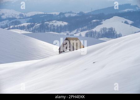 Una pittoresca scena invernale caratterizzata da una cabina in legno circondata da colline innevate. Foto Stock