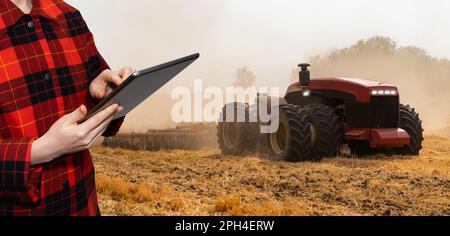 Un agricoltore con tablet digitale controlla un trattore autonomo in un'azienda agricola intelligente. Foto di alta qualità Foto Stock