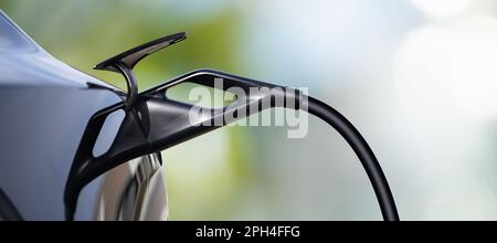 Primo piano dell'ingresso dell'auto elettrica con un cavo di ricarica collegato su sfondo verde. Foto Stock