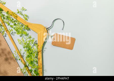 Concetto di shopping, acquisto o vendita sostenibile ed ecologico. Eco-friendly still life con appendiabiti in legno con rami verdi e etichetta vuota sul retro blu Foto Stock