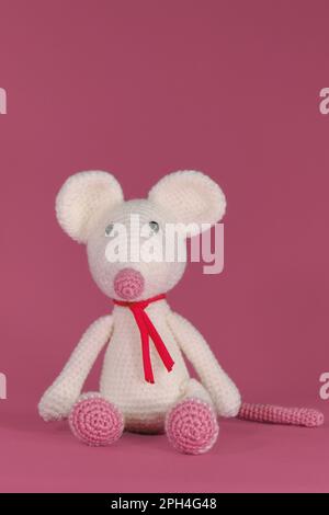 Amigurumi un mouse bianco con grandi orecchie e naso lungo su sfondo rosa. Un morbido giocattolo fai da te in cotone naturale e lana. Carino piccolo ratto accovacciato Foto Stock