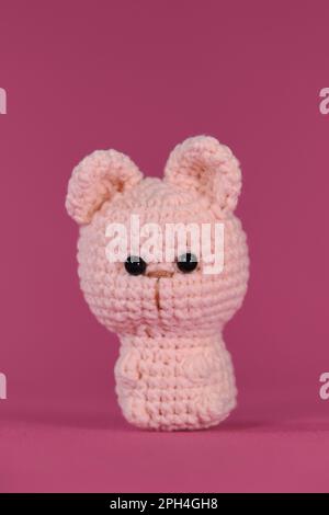 Amigurumi un piccolo gattino carino seduto su sfondo rosa. Soffice giocattolo fai da te in cotone naturale e lana. Gatto uncinetto, arte fatta a mano Vista frontale. Foto Stock