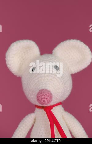 Amigurumi un mouse bianco con grandi orecchie e naso lungo su sfondo rosa. Un morbido giocattolo fai da te in cotone naturale e lana. Carino piccolo ratto accovacciato Foto Stock