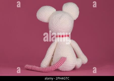 Amigurumi un mouse bianco con grandi orecchie e naso lungo su sfondo rosa. Un morbido giocattolo fai da te in cotone naturale e lana. Carino piccolo ratto accovacciato Foto Stock