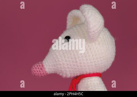 Amigurumi un mouse bianco con grandi orecchie e naso lungo su sfondo rosa. Un morbido giocattolo fai da te in cotone naturale e lana. Carino piccolo ratto accovacciato Foto Stock