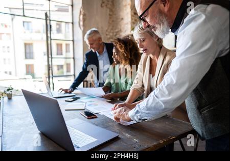 Un team di professionisti di mezza età è accoccolato intorno a un tavolo della sala conferenze, profondamente impegnato nell'analisi dei dati di una campagna di marketing che essi Foto Stock