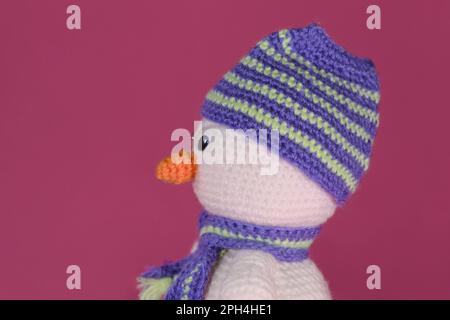 Soffice giocattolo fai da te in cotone naturale e lana. Uncinetto, arte fatta a mano Amigurumi un piccolo pupazzo di neve bianco con naso arancione e cappello a righe e sciarpa Foto Stock