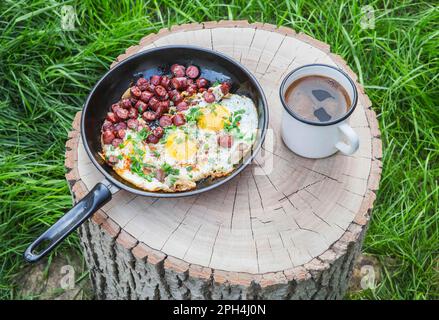 uova strapazzate con salsiccia e caffè su un ceppo nella foresta Foto Stock