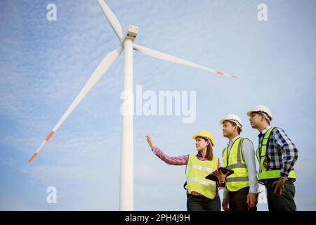 Team di ingegneri asiatici che discutono e controllano le turbine nella fattoria di turbine eoliche. Tecnologia e sostenibilità delle energie rinnovabili. Foto Stock