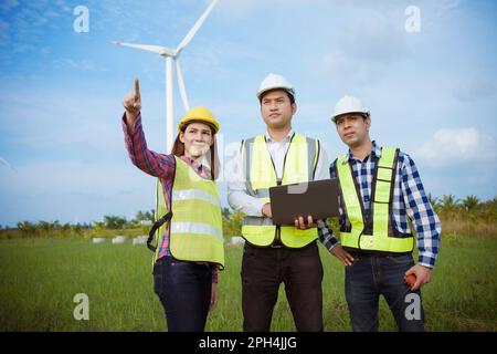 Team di ingegneri asiatici che discutono e controllano le turbine nella fattoria di turbine eoliche. Tecnologia e sostenibilità delle energie rinnovabili. Foto Stock