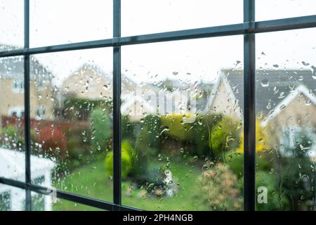 La pioggia cade sul vetro come si vede da una finestra del piano superiore. Guardando fuori ad un giardino ornato durante un rainstorm. Foto Stock