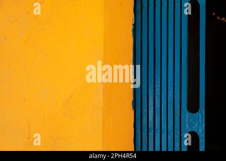 Sfondo astratto giallo e blu diviso in due metà verticalmente. Parete dai colori vivaci e cancello pieghevole di una casa vietnamita Foto Stock