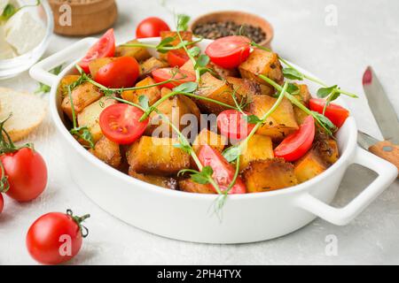 Patate fritte con ciliegia fresca e microgreens in una teglia da forno in ceramica su sfondo chiaro. Vista laterale, primo piano. Foto Stock