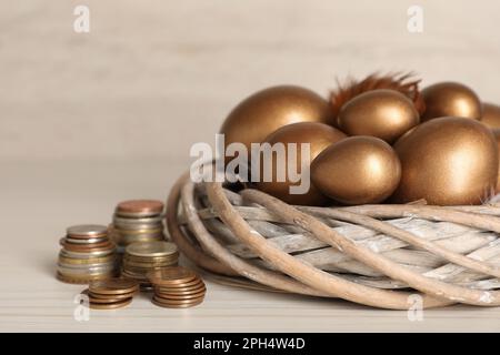 Uova d'oro in nido e monete su tavola di legno bianco. Concetto di pensione Foto Stock