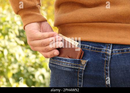 Uomo mettere portafoglio con soldi in tasca di jeans all'aperto, primo piano Foto Stock