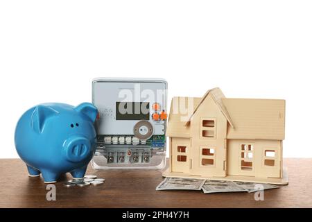 Contatore elettrico, modello di casa e banco di porcellini su tavolo di legno su sfondo bianco Foto Stock