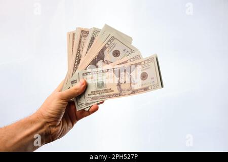 Mano dell'uomo che tiene un mucchio di dollari nella forma di un ventilatore, su uno sfondo bianco. Foto Stock