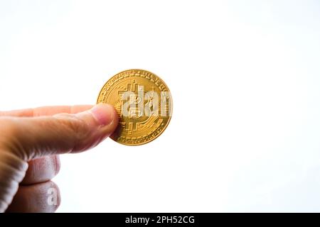 Mano dell'uomo che tiene una moneta di bitcoin con due dita, su uno sfondo bianco. Foto Stock