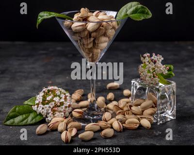 I pistacchi sono contenuti in un bicchiere trasparente e posti sul tavolo, con fiori primaverili Foto Stock