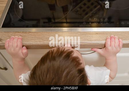 Il bambino salite su una stufa elettrica calda nella cucina domestica. Un bambino piccolo tocca la superficie della stufa con la mano al rischio di ottenere b Foto Stock