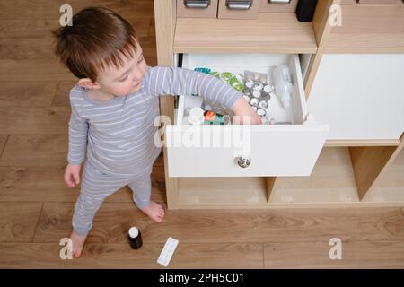 Il bambino del bambino ha aperto il cassetto dell'armadietto con le pillole e la medicina. Bambino che tiene una confezione di pillole nel salotto di casa. Bambino di età un anno nove mese Foto Stock