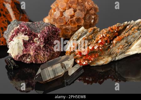 Foto ravvicinata del Gruppo delle pietre e dei minerali, tra cui Vanadinite su Barite, Aragonite Sputnik, cristalli di Erythrite su superficie riflettente Foto Stock
