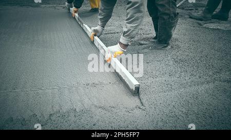 Lavori in loco con cazzuola. Lavoratori livella mortaio di cemento. Operai di costruzione usa cazzuola per livellare massetto di Malta di cemento. Lavori concreti su costr Foto Stock