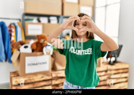 Adorabile ragazza che indossa uniforme volontaria facendo il simbolo del cuore con le mani al centro di carità Foto Stock