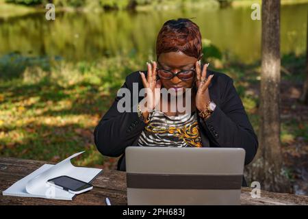 Donna d'affari che indossa i suoi occhiali. È seduta su una panchina del parco mentre è al lavoro Foto Stock