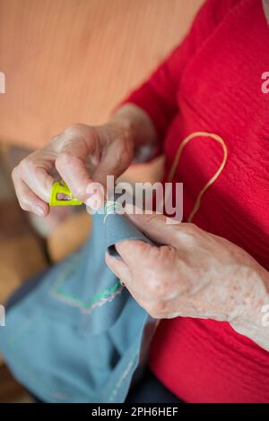 Donna anziana irriconoscibile che fa ricami con un ditale giallo. Interno Foto Stock