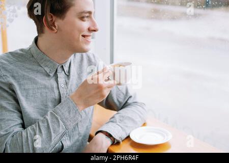 un uomo sorridente si diverte a gustare una tazza di caffè, rilassato e rilassante Foto Stock