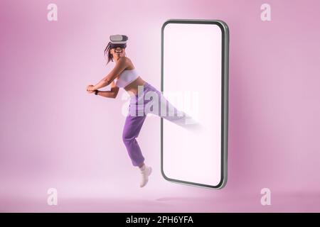 App fitness. Donna nera che gioca a tennis in realtà virtuale googles, saltando da smartphone, sfondo neon rosa Foto Stock