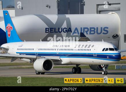 Amburgo, Germania. 24th Mar, 2023. Un Airbus 'Beluga XL' n° 4 del tipo A330-743L è atterrato all'aeroporto di Finkenwerder e, dopo aver lasciato la pista, sta guidando la punta-prima in un edificio di fabbrica. Il bimotore trasporta parti di aeromobili tra i siti di produzione di Airbus e anche alla Airbus Operations GmbH a sud-ovest di Amburgo. In primo piano, un Airbus A321-200Neo gestito da China Southern sta dirigendo verso la pista. Credit: Soeren Stache/dpa/Alamy Live News Foto Stock