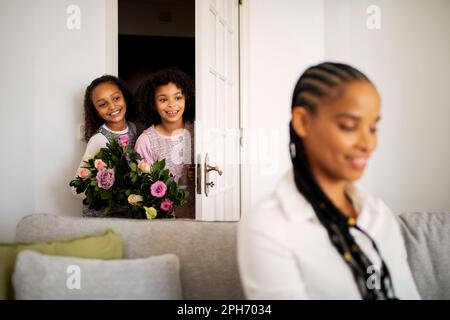 African Kids Girls che tiene i fiori in piedi dietro la schiena della mamma all'interno Foto Stock