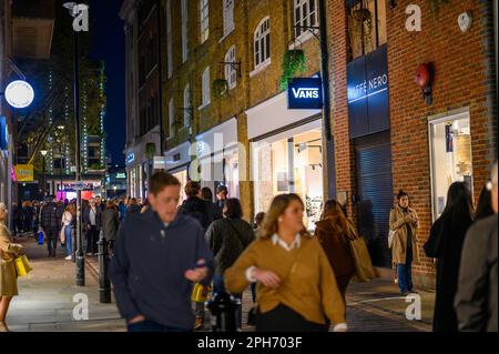 LONDRA - 12 novembre 2022: Un'affollata scena di strada londinese di notte fuori da un negozio di furgoni. Il negozio luminoso attira una grande folla di acquirenti e. Foto Stock