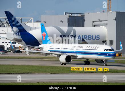 Amburgo, Germania. 24th Mar, 2023. Un Airbus 'Beluga XL' n° 4 del tipo A330-743L è atterrato all'aeroporto di Finkenwerder e, dopo aver lasciato la pista, sta guidando la punta-prima in un edificio di fabbrica. Il bimotore trasporta parti di aeromobili tra i siti di produzione di Airbus e anche alla Airbus Operations GmbH a sud-ovest di Amburgo. In primo piano, un Airbus A321-200Neo gestito da China Southern sta dirigendo verso la pista. Credit: Soeren Stache/dpa/Alamy Live News Foto Stock