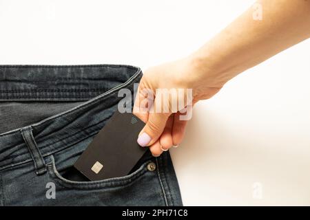 La mano di una donna toglie una carta di credito da una tasca di jeans, denaro Foto Stock