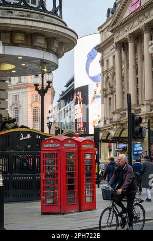 LONDRA - 13 novembre 2022: Un uomo passa accanto alle tradizionali cabine telefoniche rosse in una delle intersezioni più trafficate di Londra, la vibrante Piccadill Foto Stock