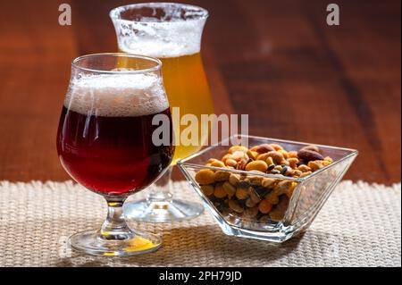 Bicchieri di birra belga bionda gialla e bruna scura preparati in abbazia serviti al bar con noci da festa, primo piano Foto Stock