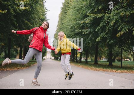 Madre e figlio saltano nel parco autunnale. Stagione autunnale. Felice giovane bella madre e suo figlio hanno una passeggiata nel parco Foto Stock